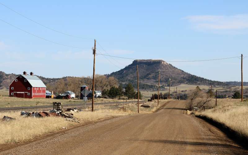 A view of Greenland with a red barn and other ranch infrastructure sits on flat land near a train track with foothills in the background
